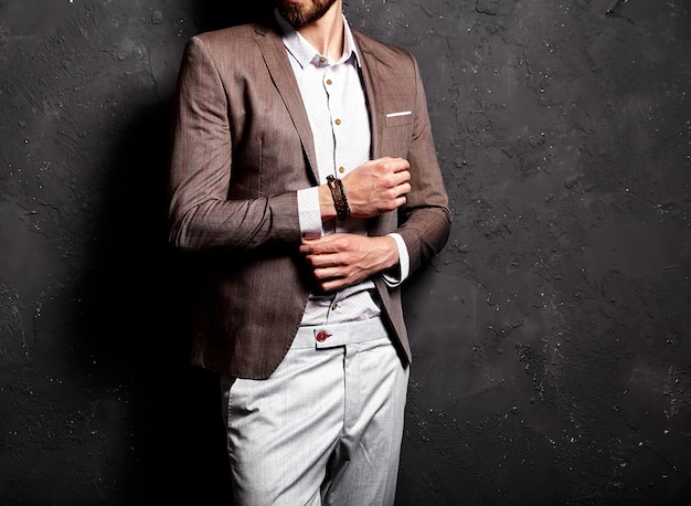 Портрет красивого модного стильного хипстерского бизнесмена, одетого в элегантный коричневый костюм возле темной стены