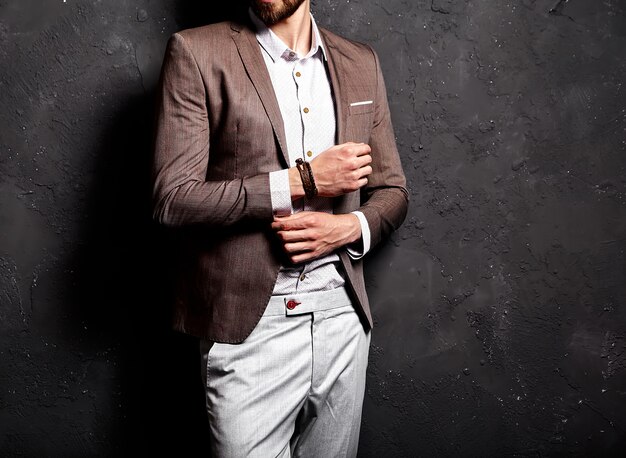 portrait of handsome fashion stylish hipster businessman model dressed in elegant brown suit near dark wall