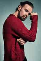 Free photo portrait of handsome fashion stylish hipster model dressed in warm red sweater  posing in studio.