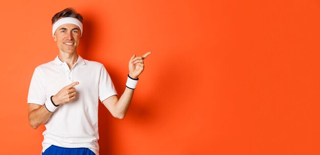 Portrait of handsome fit male athlete in headband and white tshirt pointing fingers at upper right c