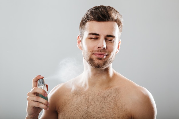 Portrait of a handsome half naked man spraying perfume