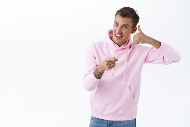 Portrait of handsome happy young man, pointing finger and shows phone gesture