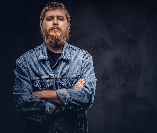 Free photo portrait of a handsome hipster guy dressed in jeans jacket posing with crossed arms. isolated on a dark background.