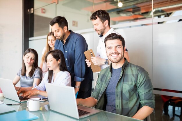 Portrait of handsome latin man in casuals sitting with colleagues working at the back