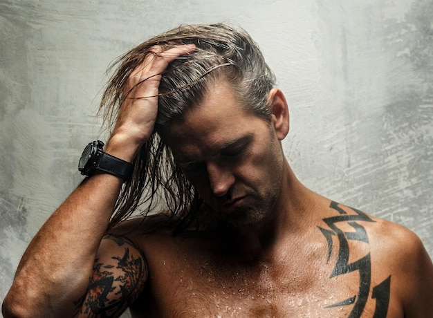 Portrait of handsome long-haired man with naked torso. Isolated on gray background. Tattoed male body.