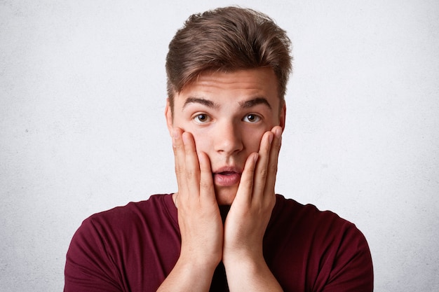 Free photo portrait of handsome male scratches cheeks and looks with puzzlement at camera