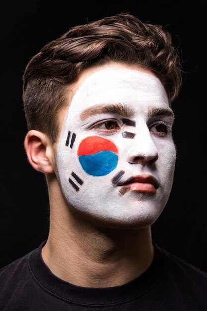 검은 배경에 고립 된 페인트 플래그 얼굴로 대한민국 대표팀의 잘 생긴 남자 얼굴 팬 팬의 초상화. 팬들의 감정.