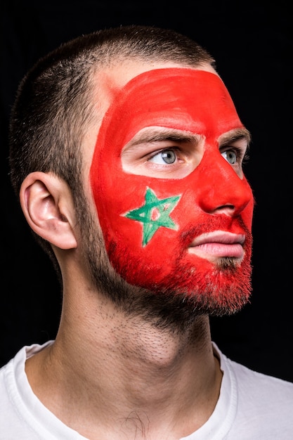 黒の背景に分離された塗られた旗の顔とモロッコ代表のハンサムな男の顔サポーターファンの肖像画。ファンの感情。