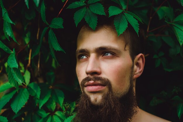 Портрет красивый человек на зеленых летних листьев. Мода Брюнетка человек с голубыми глазами, портрет в диких листьях (виноград), естественный фон.