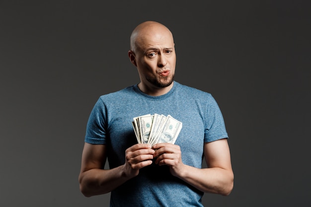 Portrait of handsome man in grey shirt holding money over dark wall