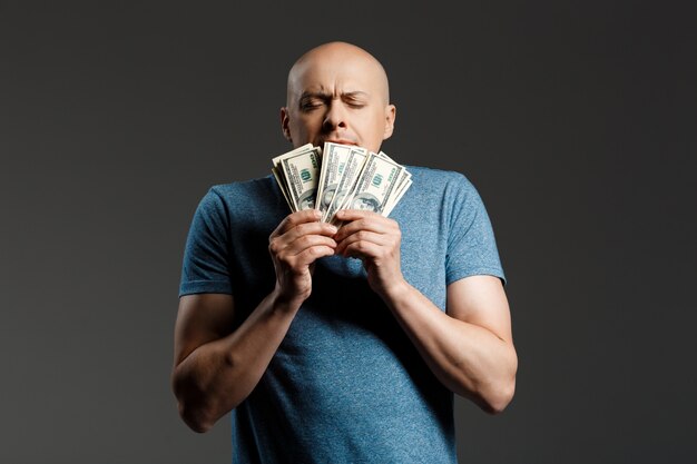 Portrait of handsome man in grey shirt holding money over dark wall