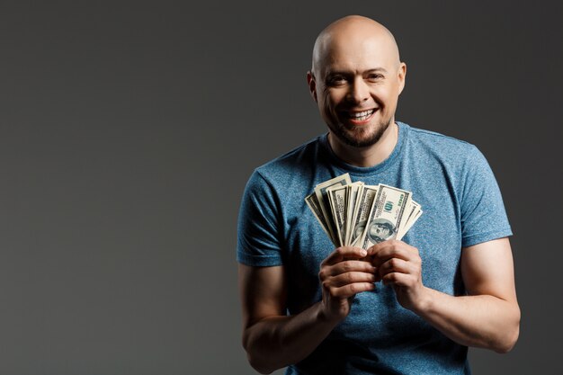 Portrait of handsome man in grey shirt holding money over dark wall