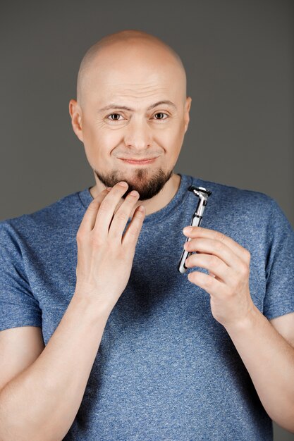 Portrait of handsome man in grey shirt holding razor over dark wall