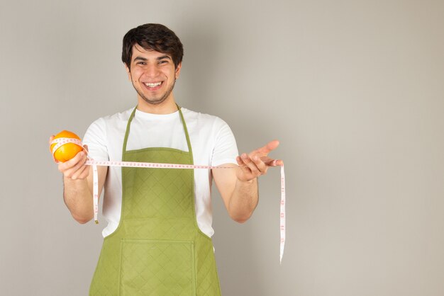 Ritratto di un bell'uomo modello in grembiule che tiene un frutto arancione.