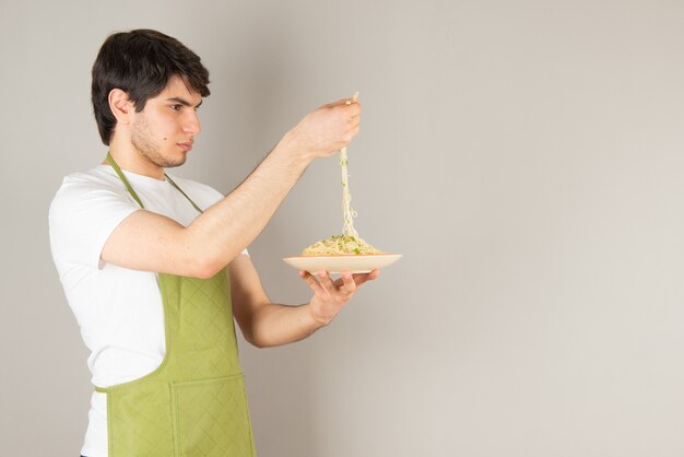 Portrait of a handsome man model in apron holding a plate with food.