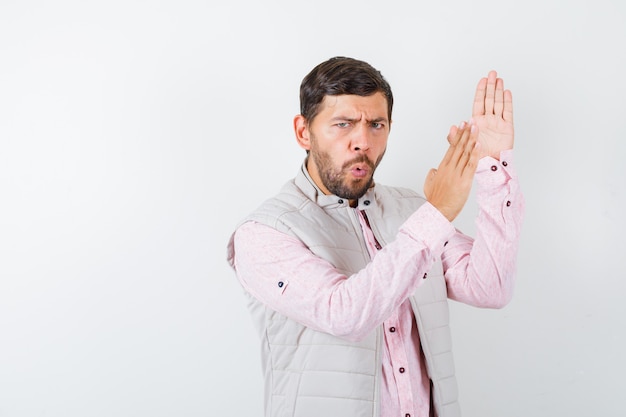 Portrait of handsome man showing karate chop gesture in vest, shirt and looking enraged 