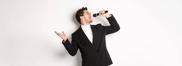 Портрет красивого мужчины, страстно поющего песню, стоящего в черном костюме с микрофоном и п