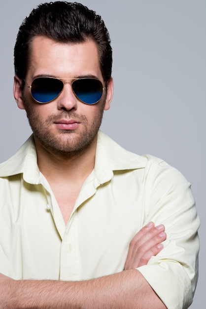 Free photo portrait of handsome man in yellow shirt wearing sunglasses with crossed arms poses