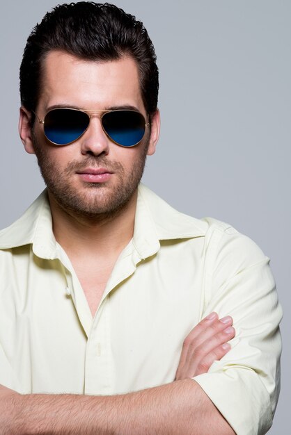 Portrait of handsome man in yellow shirt wearing sunglasses with crossed arms poses 