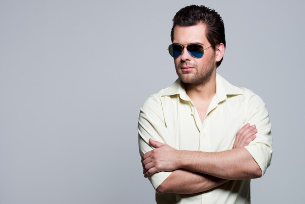 Portrait of handsome man in yellow shirt wearing sunglasses with crossed arms poses 