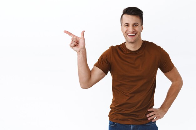 Portrait of handsome masculine young man pointing finger at copy space