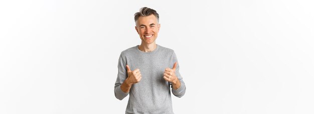 Portrait of handsome middleaged guy with grey hairstyle showing thumbsup and smiling approve something good like idea standing over white background