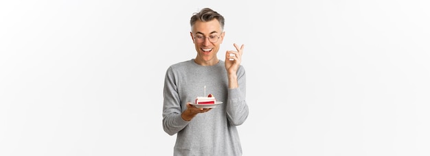 Portrait of handsome middleaged man smiling and looking amazed at birthday cake with lit candle maki