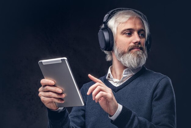 Portrait of a handsome senior man using a tablet with headphones in a studio over a dark background.