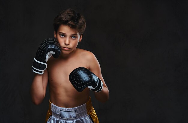 카메라를 보고 장갑을 끼고 잘생긴 벗은 젊은 권투 선수의 초상화. 어두운 배경에 고립.