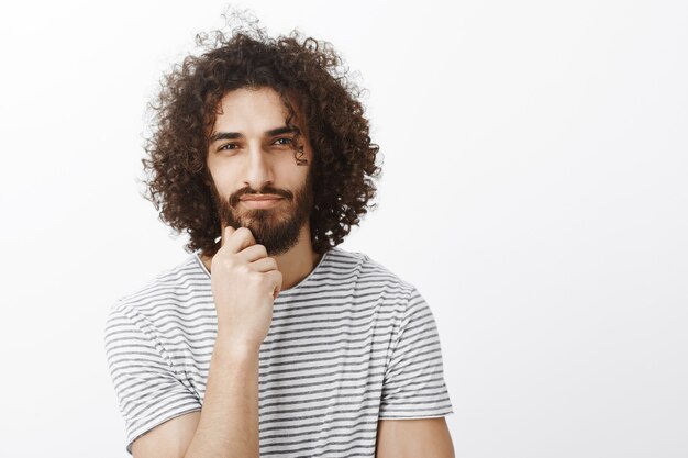 Portrait of handsome smart and creative hispanic guy with afro haircut, holding hand on chin