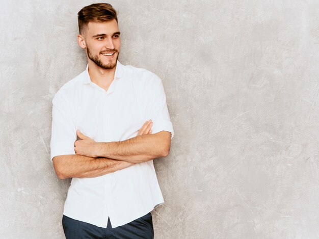 Ritratto del modello sorridente bello dell'uomo d'affari dei pantaloni a vita bassa che porta la camicia bianca casuale di estate. braccia incrociate