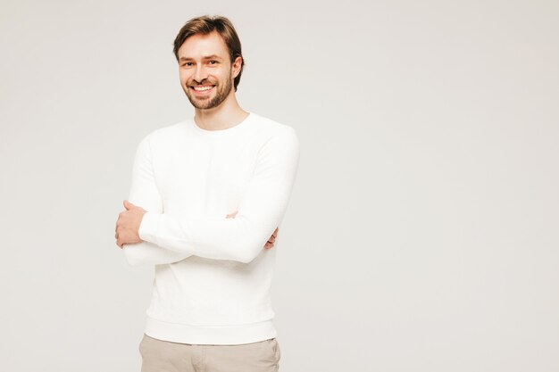 Portrait of handsome smiling hipster lumbersexual businessman model wearing casual white sweater and trousers