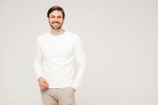 Portrait of handsome smiling hipster lumbersexual businessman model wearing casual white sweater and trousers