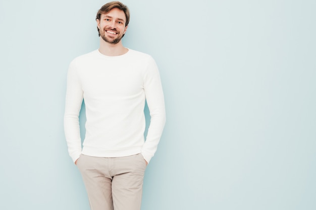 Portrait of handsome smiling hipster lumbersexual businessman model wearing casual white sweater and trousers