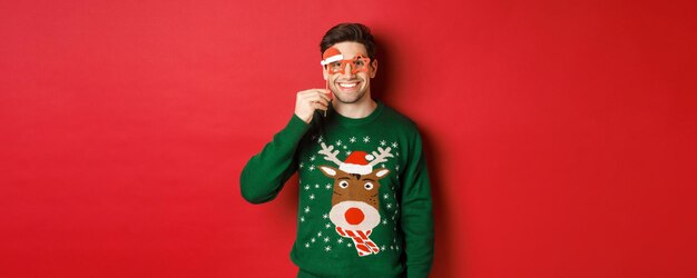Portrait of handsome smiling man in christmas sweater and party glasses celebrating new year and hav...