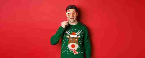 Free photo portrait of handsome smiling man in christmas sweater and party glasses looking surprised and happy