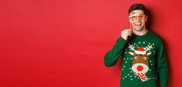 크리스마스 스웨터와 파티 안경을 쓰고 놀라고 행복해 보이는 잘생긴 웃는 남자의 초상화...