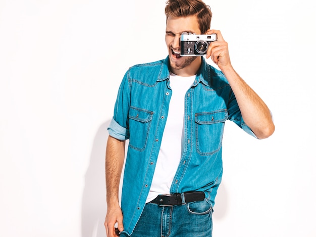 Il ritratto dei vestiti d'uso d'uso dei jeans dell'estate sorridente bello. maschera di presa maschio di modello sulla vecchia macchina fotografica d'annata della foto.