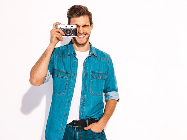 Portrait of handsome smiling man wearing summer jeans clothes. Model male taking picture on old vintage photo camera. 