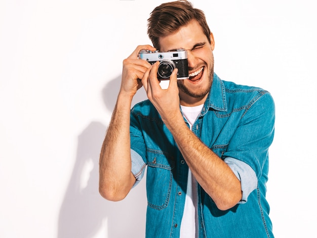 Portrait of handsome smiling man wearing summer jeans clothes. Model male taking picture on old vintage photo camera. 
