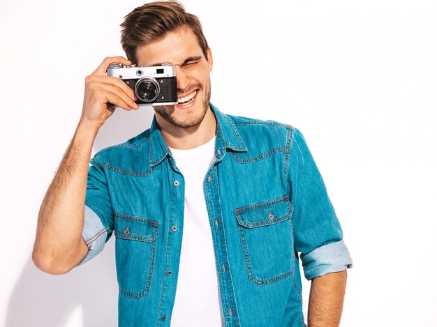 Портрет красавец улыбающегося носить летние джинсы одежды. Модельный мужчина фотографируя на старой винтажной камере фото.