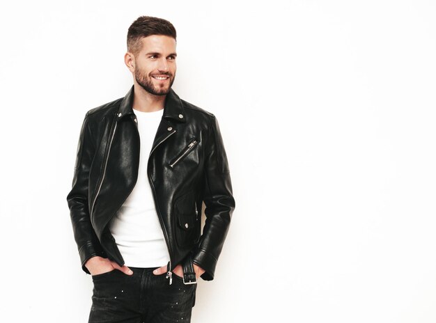 Portrait of handsome smiling model Sexy stylish man dressed in biker leather jacket and black jeans Fashion hipster male isolated on white in studio