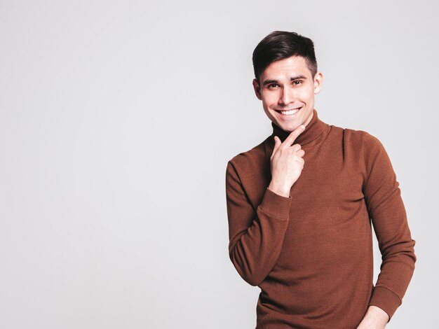 Portrait of handsome smiling model Sexy stylish man dressed in brown turtleneck sweater and jeans Fashion hipster male posing in studio