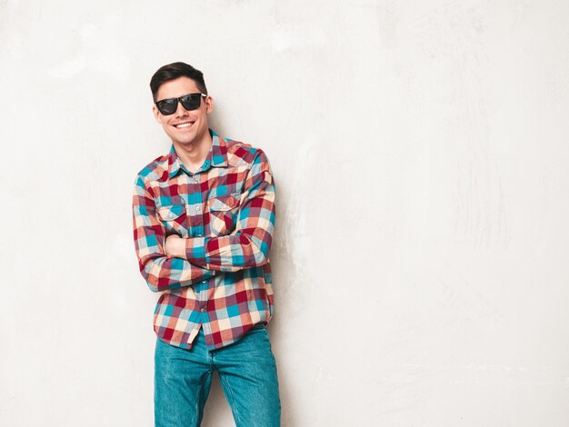 Portrait of handsome smiling model Sexy stylish man dressed in red checkered shirt and jeans Fashion hipster male posing near grey in studio Isolated