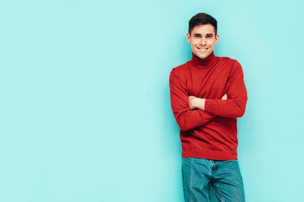 잘생긴 웃는 모델의 초상화 빨간 터틀넥 스웨터와 청바지를 입고 섹시 한 세련 된 남자 패션 힙 스터 남성 스튜디오에서 파란색 벽 근처 포즈 절연