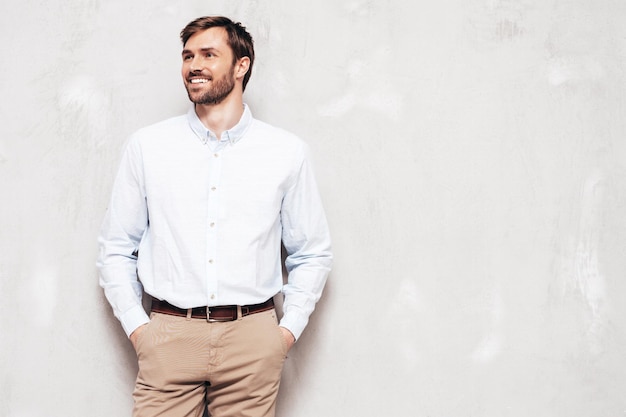 Portrait of handsome smiling model sexy stylish man dressed in shirt and trousers fashion hipster male posing near grey wall in studio isolated