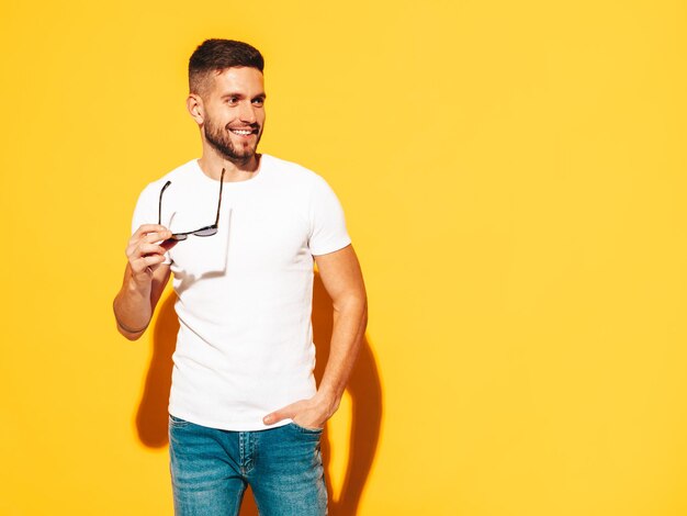 Portrait of handsome smiling model Sexy stylish man dressed in summer clothes Fashion hipster male posing near yellow wall in studio