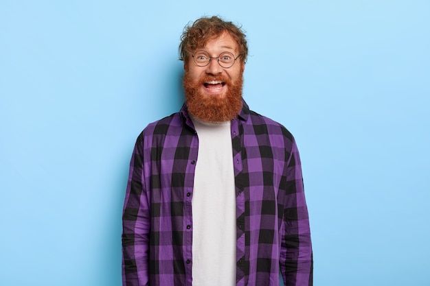 Free photo portrait of handsome smiling stylish ginger guy posing against the blue wall