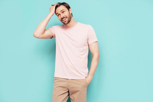 Portrait of handsome smiling stylish hipster lambersexual model Sexy man dressed in pink Tshirt and trousers Fashion male isolated on blue wall in studio