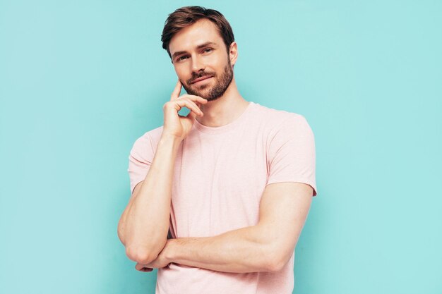 Portrait of handsome smiling stylish hipster lambersexual model Sexy man dressed in pink Tshirt and trousers Fashion male isolated on blue wall in studio